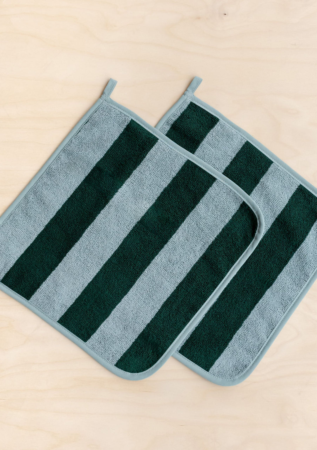 Two green striped Terry Cotton Face Cloths Set of 2 in Green Stripe by TBCo laid flat on wooden surface