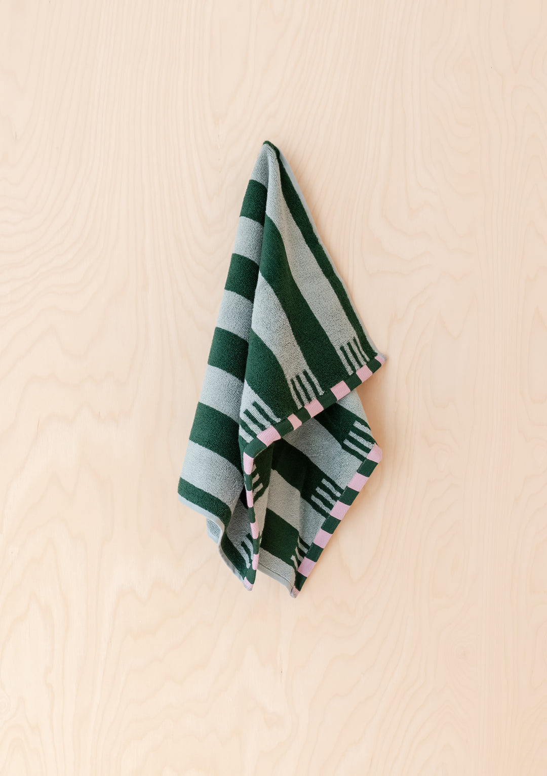 Soft and absorbent TBCo Terry Cotton Hand Towel in Green Stripe hanging against a light wooden background