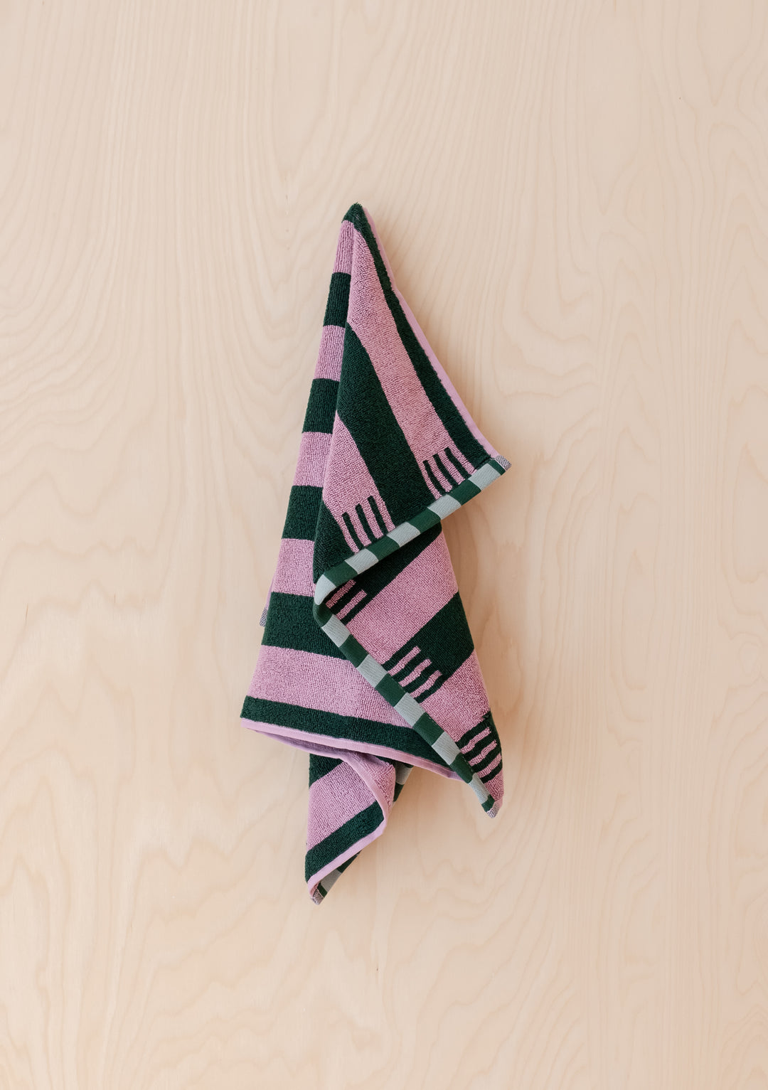 TBCo Terry Cotton Hand Towel in Rose Stripe hanging against pale wood, showing plush texture and checkerboard edges.
