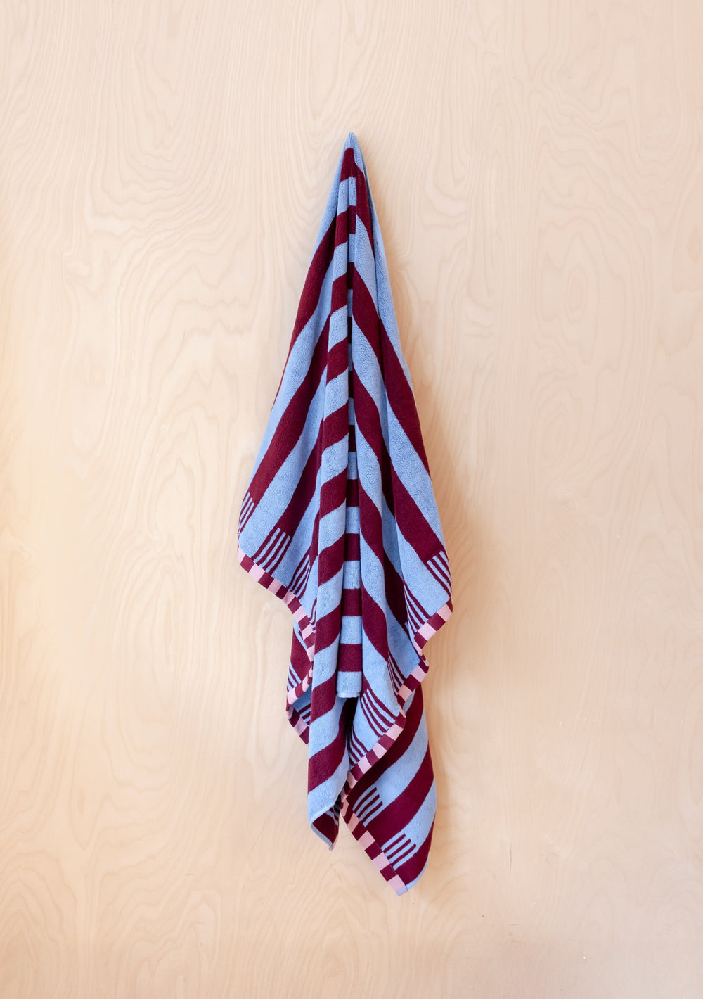 Luxurious TBCo Cotton Towels in Blue Stripe with burgundy stripes and checkerboard edges, elegantly draped against cream wall