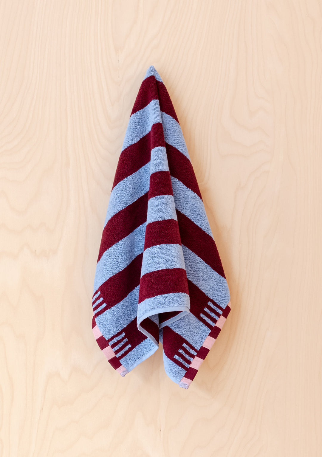 Plush TBCo Cotton Towels in Blue Stripe with burgundy stripes and pink checkered border, elegantly draped against light wooden surface