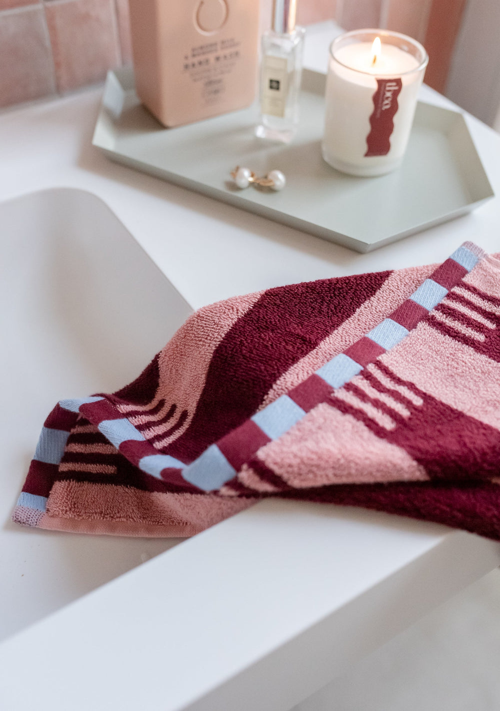 TBCo Cotton Towels in Pink Stripe with burgundy and blue checkerboard pattern, displayed on white surface with candle and bath accessories
