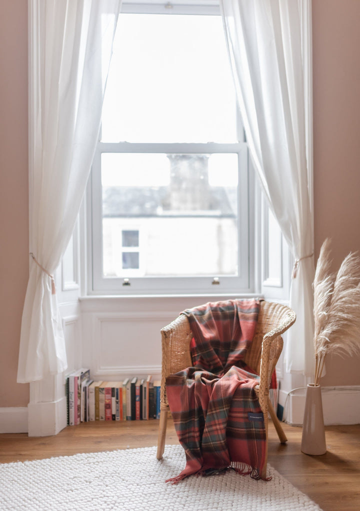 TBCo Stewart Royal Antique Tartan Lambswool Blanket draped over wicker chair by bright window with white curtains