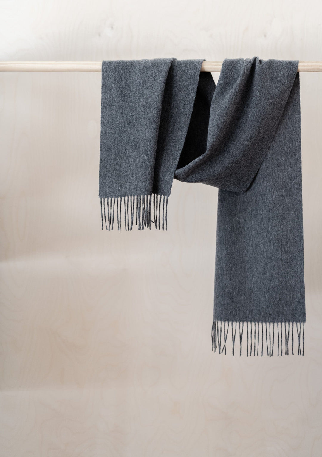 TBCo Lambswool Scarf in Charcoal Melange draped over wooden rail, showing soft texture and fringed ends