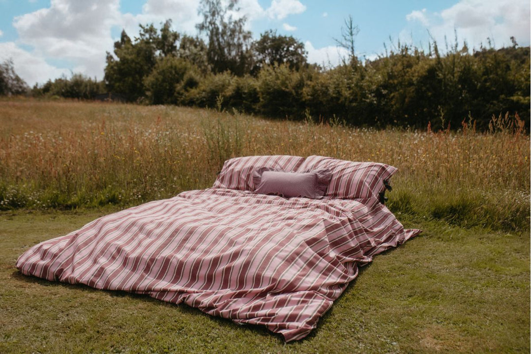 TBCo Bedding - An unmade bed, featuring TBCo's green stripe duvet cover and pillowcases, with an open magazine laid on top.