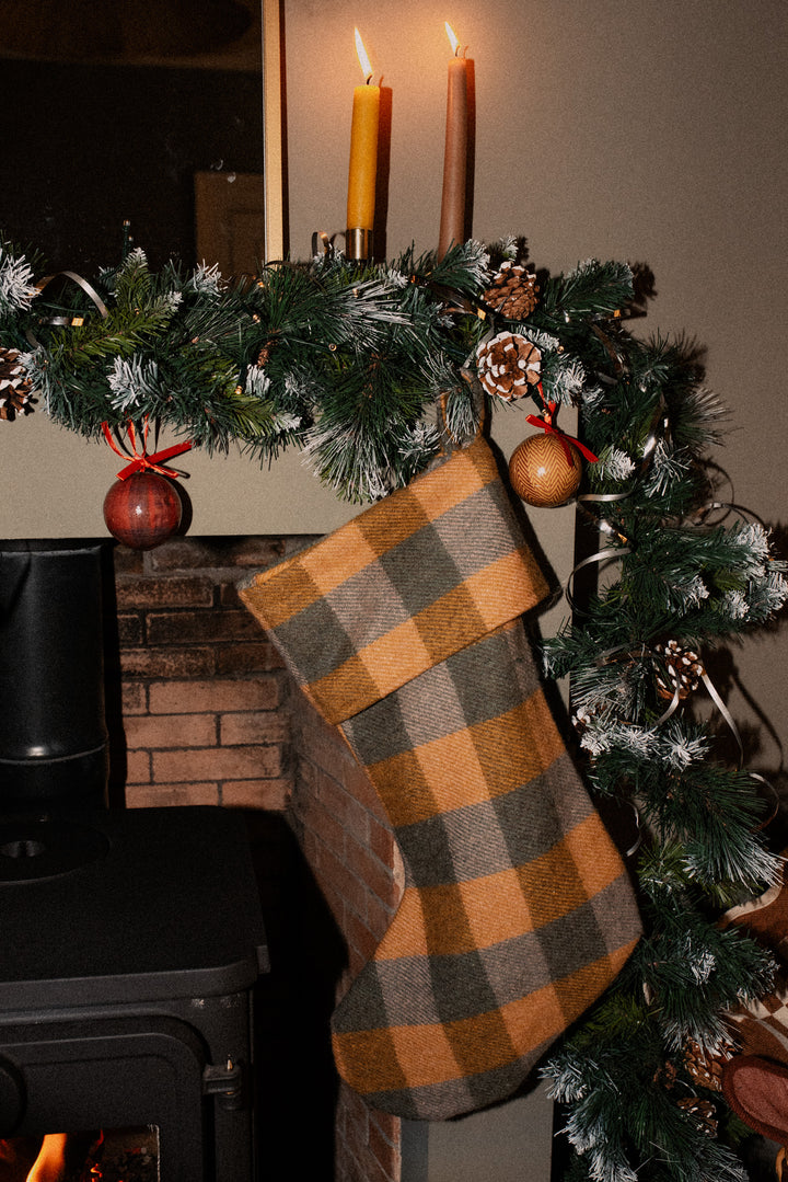 TBCo Recycled Wool Christmas Stocking in Mackellar Tartan hanging by a fireplace with festive greenery and candles above.