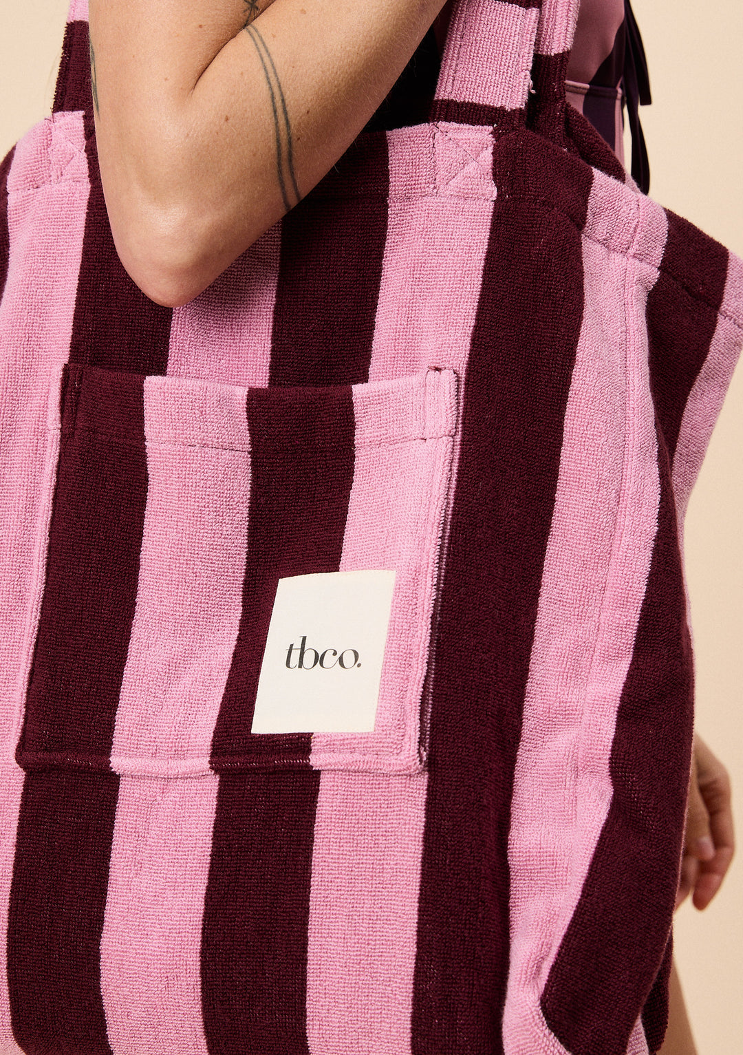 Close-up of TBCo Terry Cotton Tote Bag in Burgundy Stripe featuring soft textured vertical bands and a front pocket with logo patch