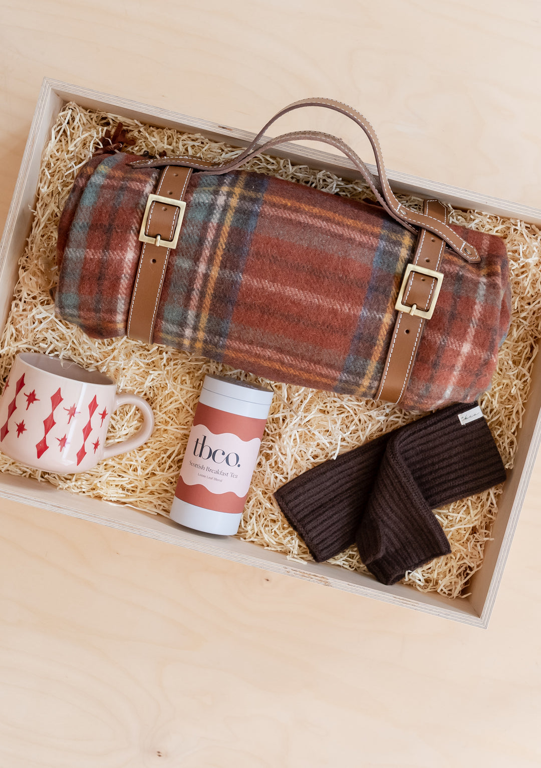 Picnic Gift Box by TBCo featuring a rolled blanket, ceramic mug, chocolate tin, and warm gloves in a wooden display box