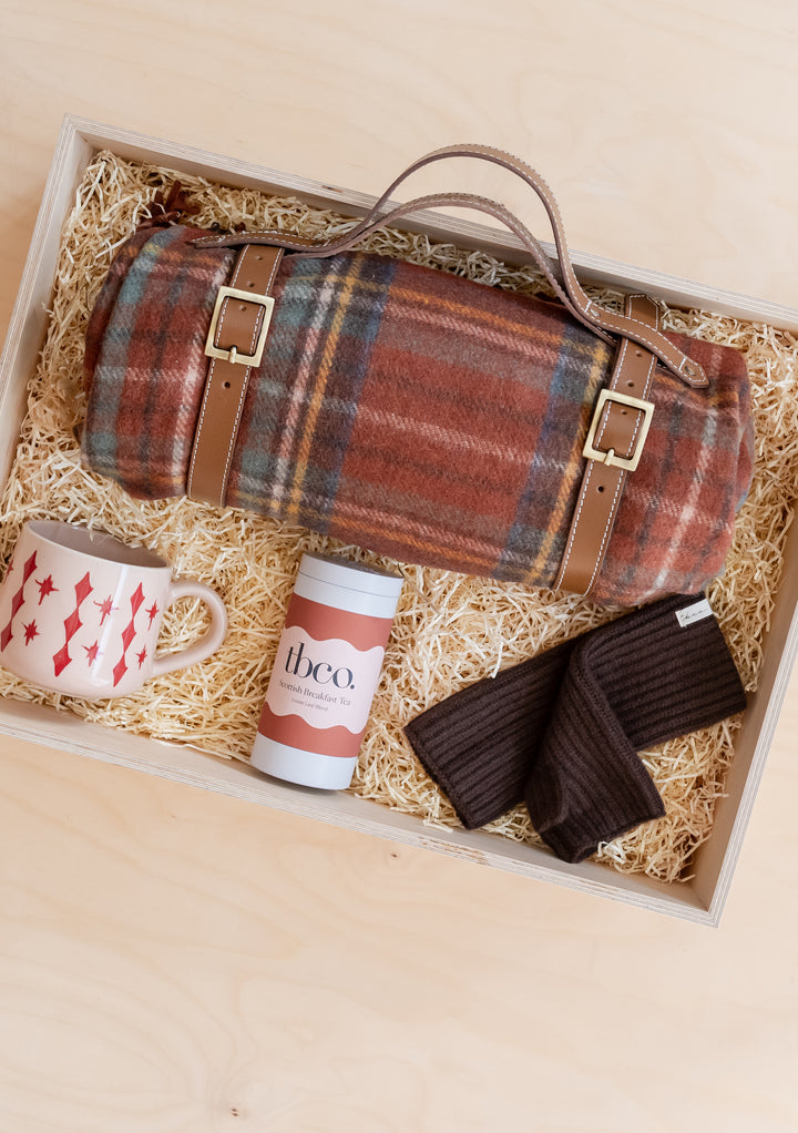 Picnic Gift Box by TBCo featuring a rolled blanket, ceramic mug, chocolate tin, and warm gloves in a wooden display box