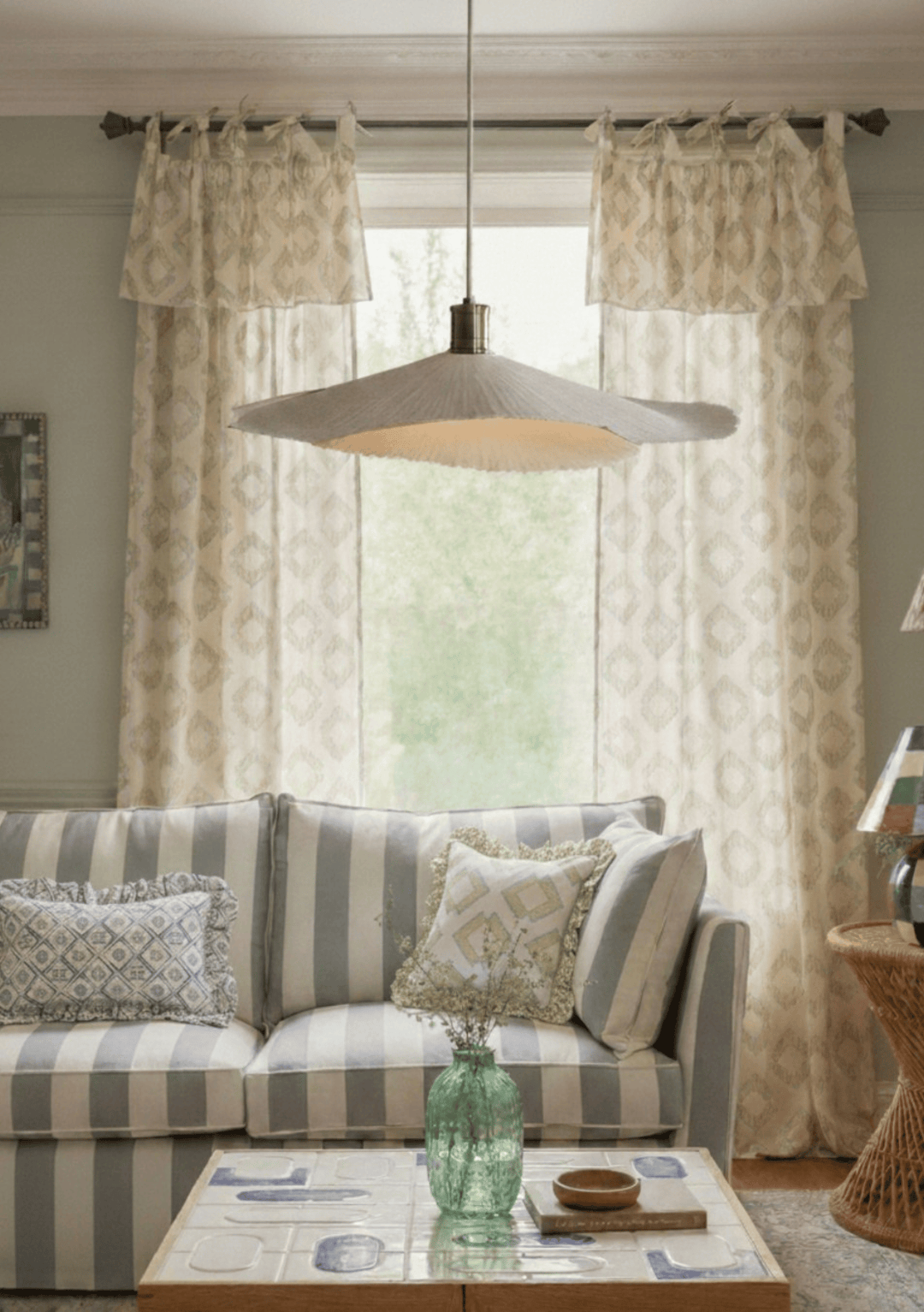 Living room with striped sofa, patterned TBCo Cotton Tie Curtains, and a hanging light fixture.