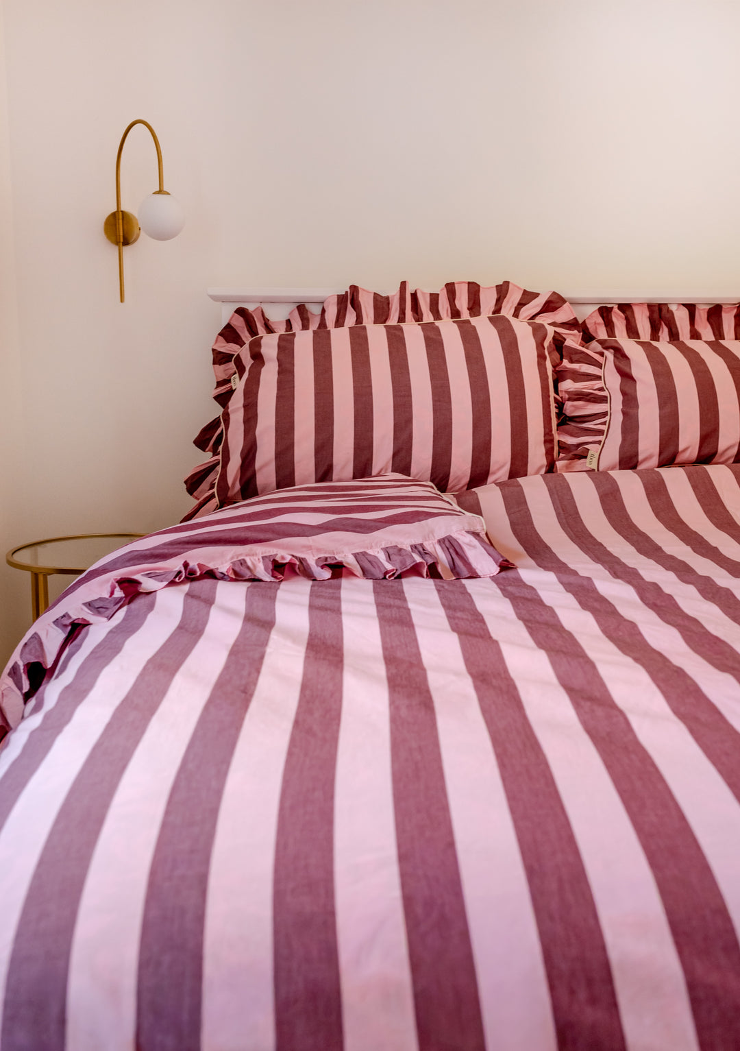 Close-up of TBCo Cotton Duvet Cover & Pillowcases Set in Pink & Burgundy Stripe with ruffle edge on bed in cosy room
