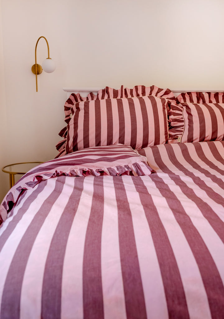 Close-up of TBCo Cotton Duvet Cover & Pillowcases Set in Pink & Burgundy Stripe with ruffle edge on bed in cosy room