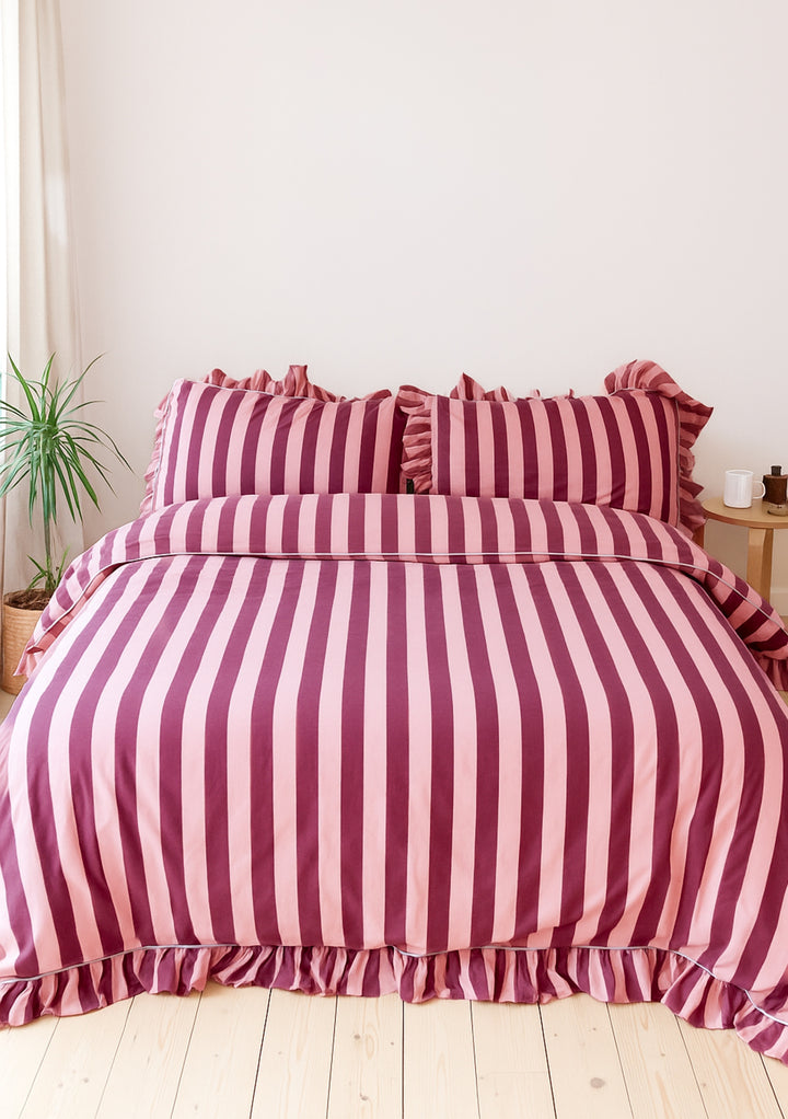 TBCo Cotton Duvet Cover & Pillowcases Set in Pink & Burgundy Stripe with ruffle edges styled on a bed in a bright room