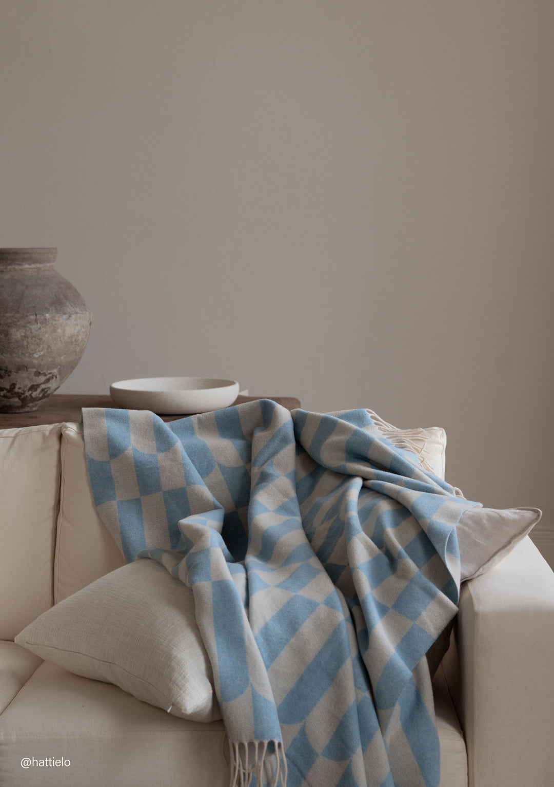 TBCo Lambswool Blanket in Blue Geo with soft fringes draped over cream sofa, showing checkered blue and beige pattern