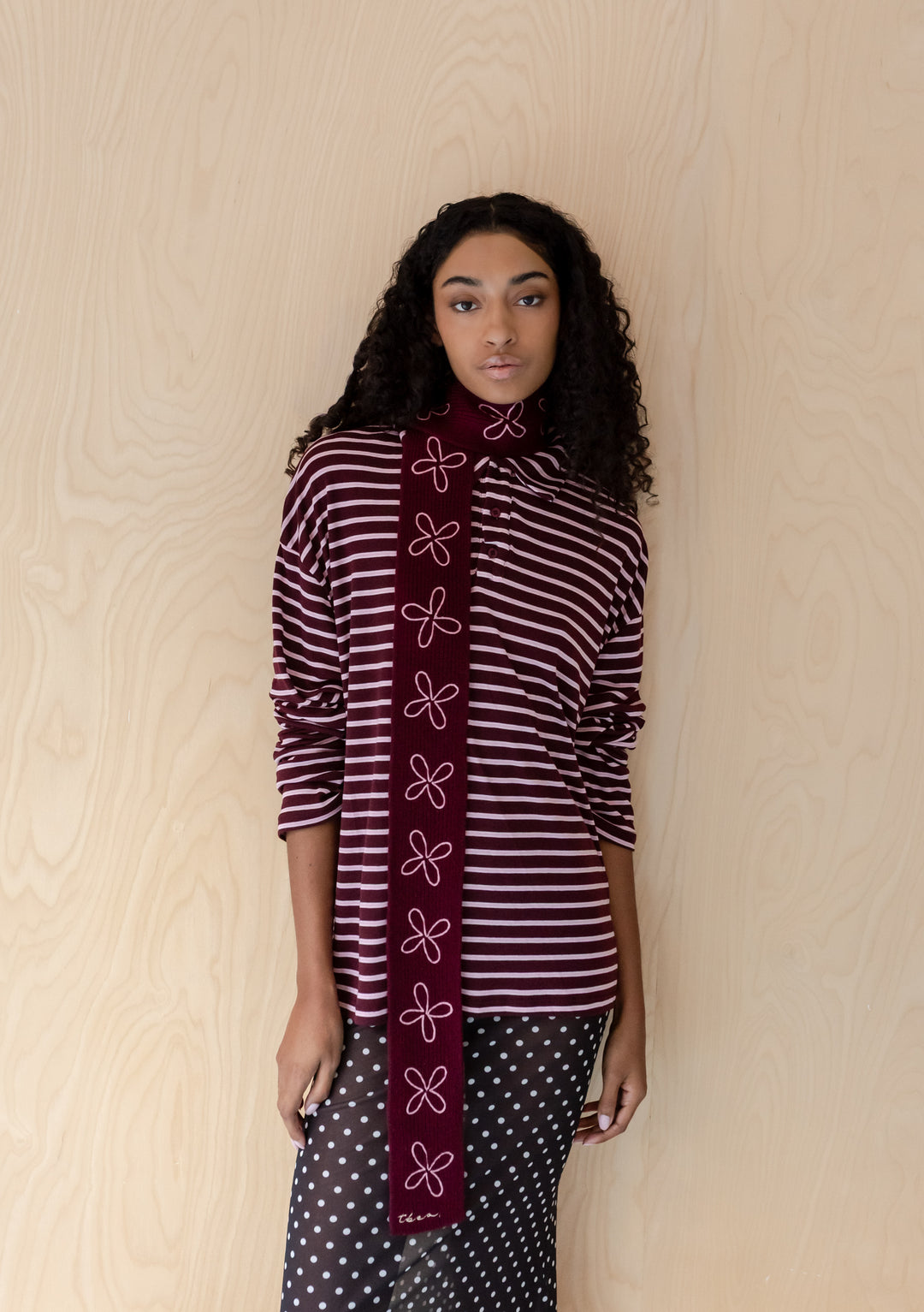 Woman wearing TBCo Merino Wool Skinny Scarf in Burgundy Flora with pale pink embroidered floral pattern against wood background