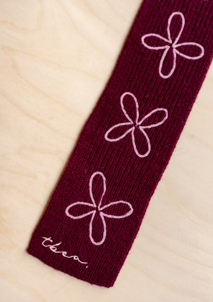 Close-up of TBCo Merino Wool Skinny Scarf in Burgundy Flora showing pale pink floral embroidery on soft ribbed fabric.