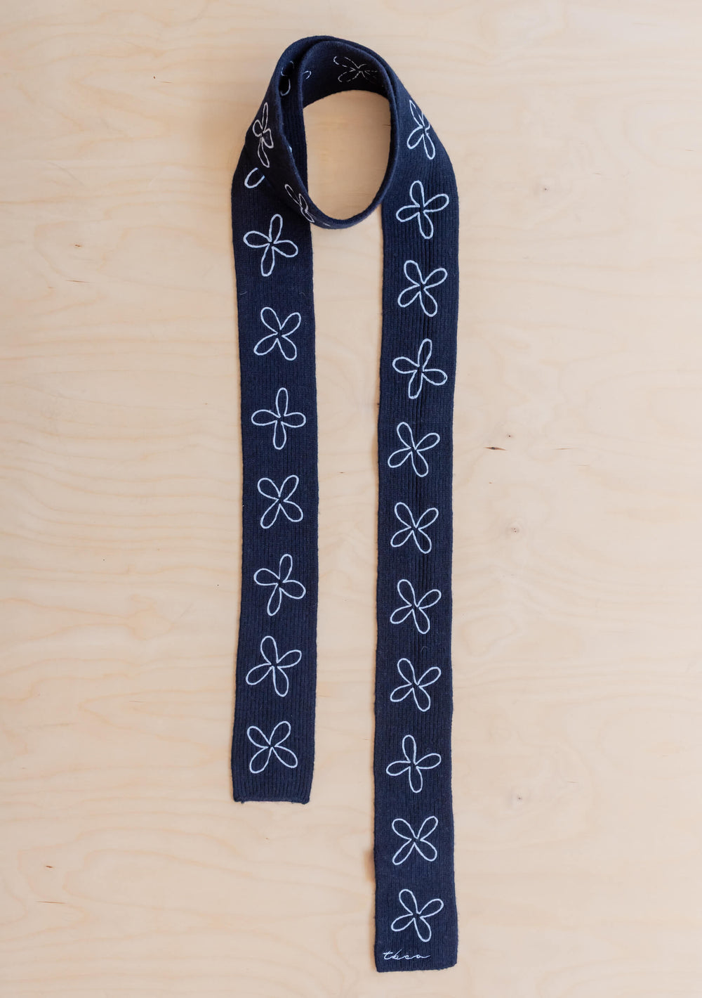TBCo Merino Wool Skinny Scarf in Navy Flora, lying on a wooden background.