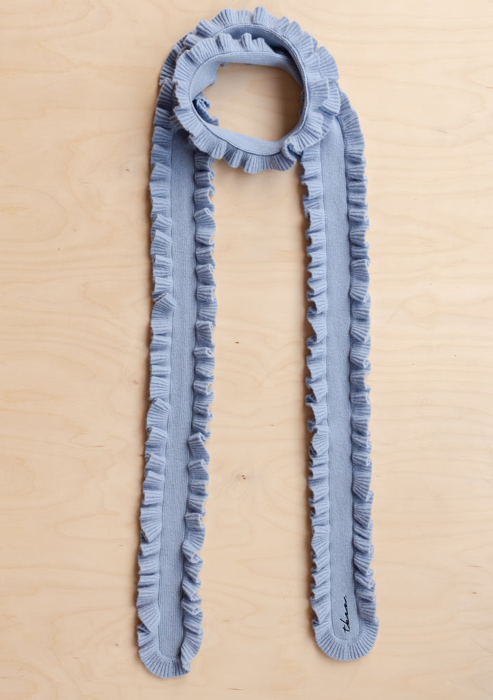 TBCo Merino Wool Skinny Scarf in Blue Ruffle laid flat on wooden surface showing ruffled edges and soft texture