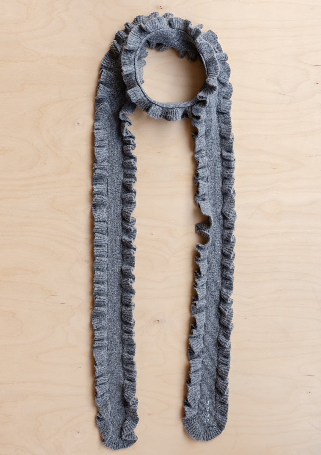 TBCo Merino Wool Skinny Scarf in Grey Ruffle laid flat on wooden surface showing ruffled edges and soft texture