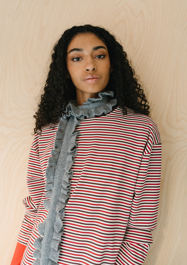Model wearing TBCo Merino Wool Skinny Scarf in Grey Ruffle with soft ruffled edges over striped top on wood background