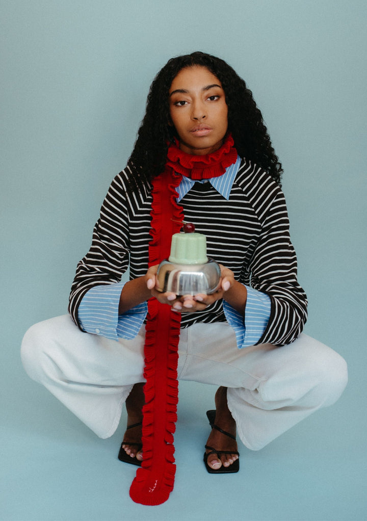 Model wearing TBCo Merino Wool Skinny Scarf in Red Ruffle with ruffled trim styled over striped top and white trousers