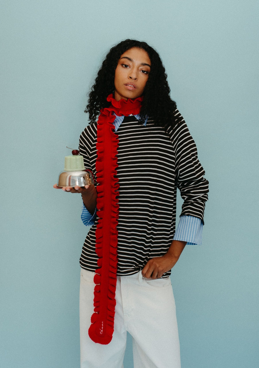 Model wearing TBCo Merino Wool Skinny Scarf in Red Ruffle with ruffled trim over striped top against pale blue background