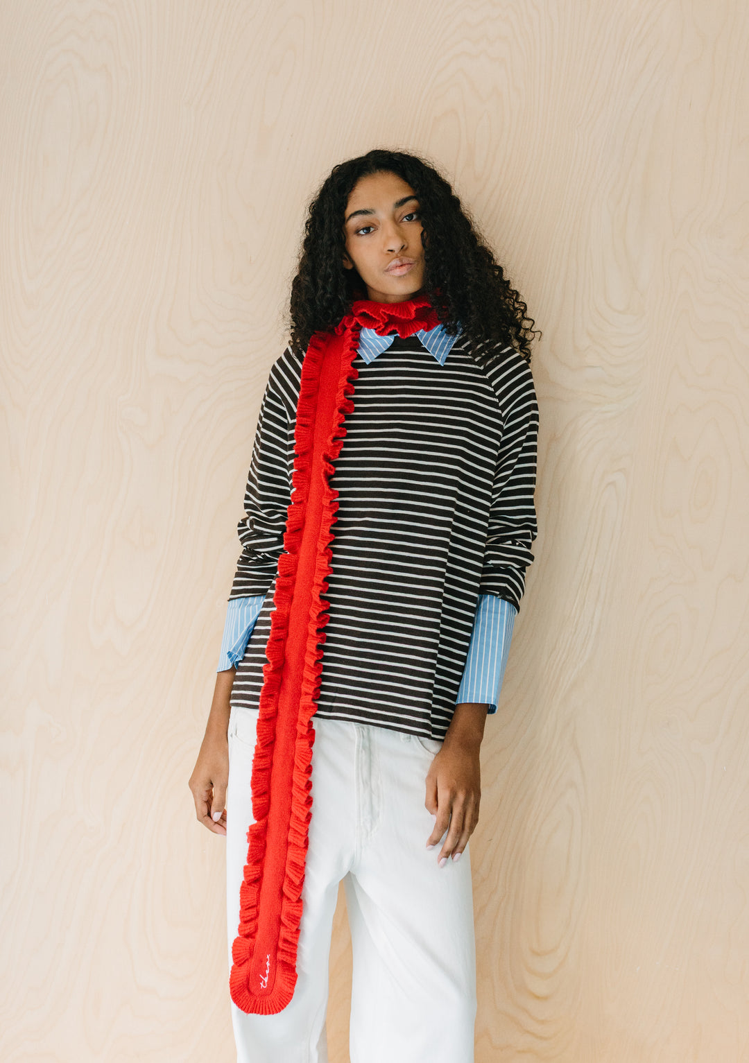 Model wearing TBCo Merino Wool Skinny Scarf in Red Ruffle with playful textured edges and vibrant red colour against striped top and white trousers