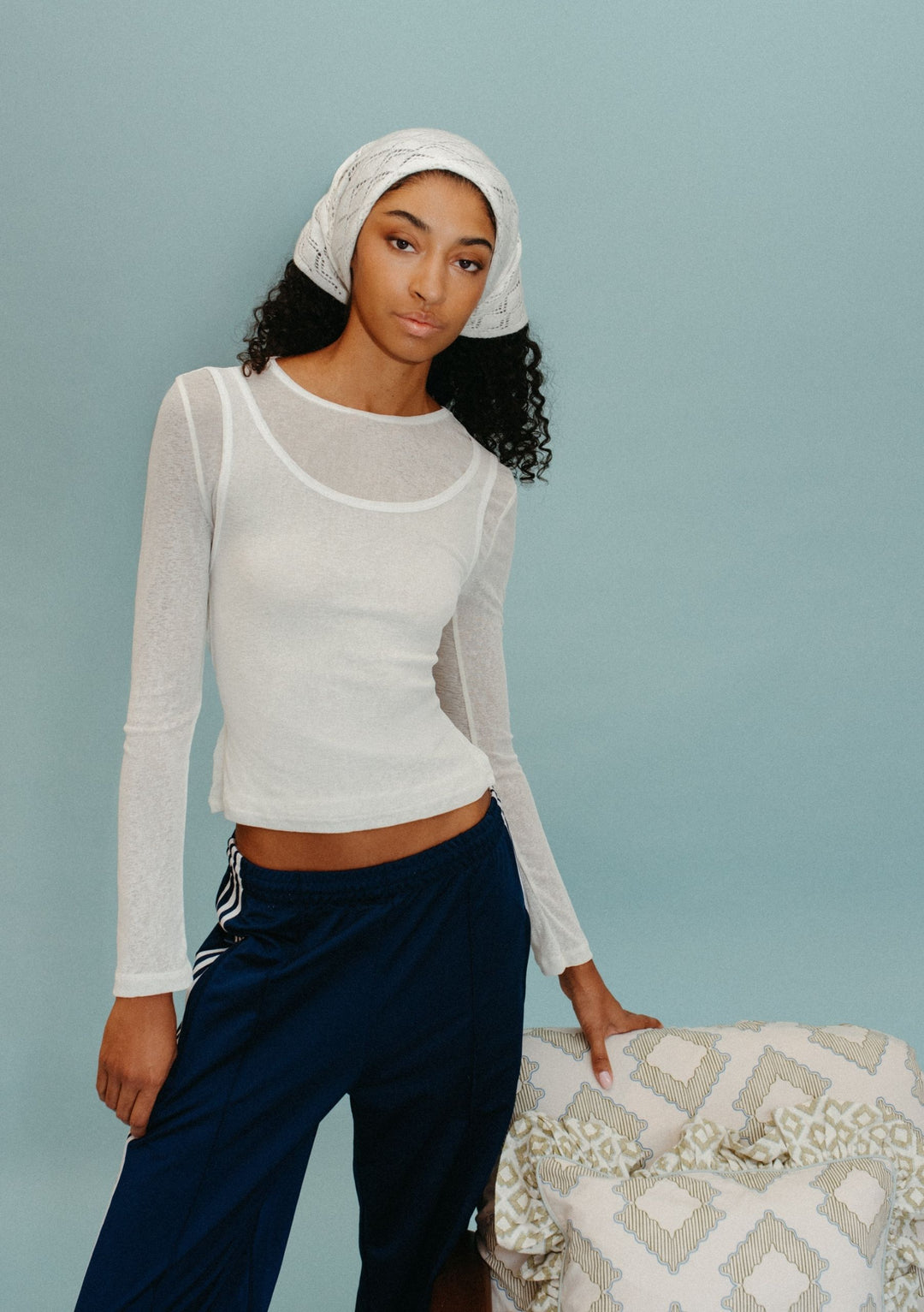 Model wearing TBCo Merino Wool Triangle Scarf in White Pointelle styled as a head wrap with sheer white top and navy trousers