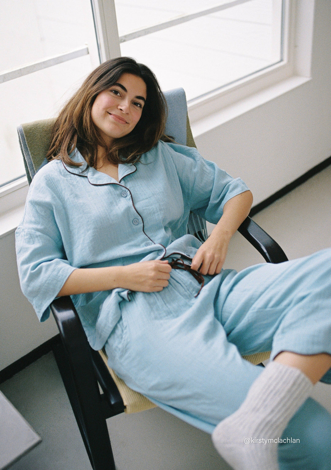 Woman relaxing in TBCo Cropped Cotton Pyjamas in Blue with brown contrast piping, soft cotton fabric details visible