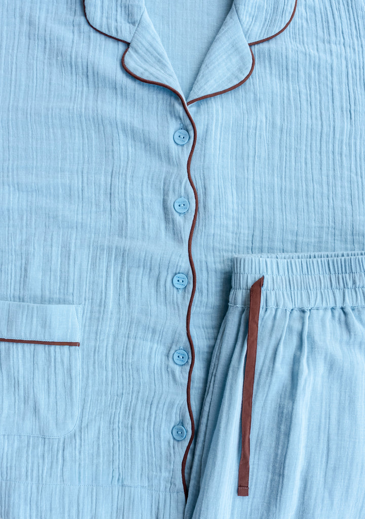 Close-up of TBCo Cropped Cotton Pyjamas in Blue showing soft fabric texture with brown contrast piping and button details