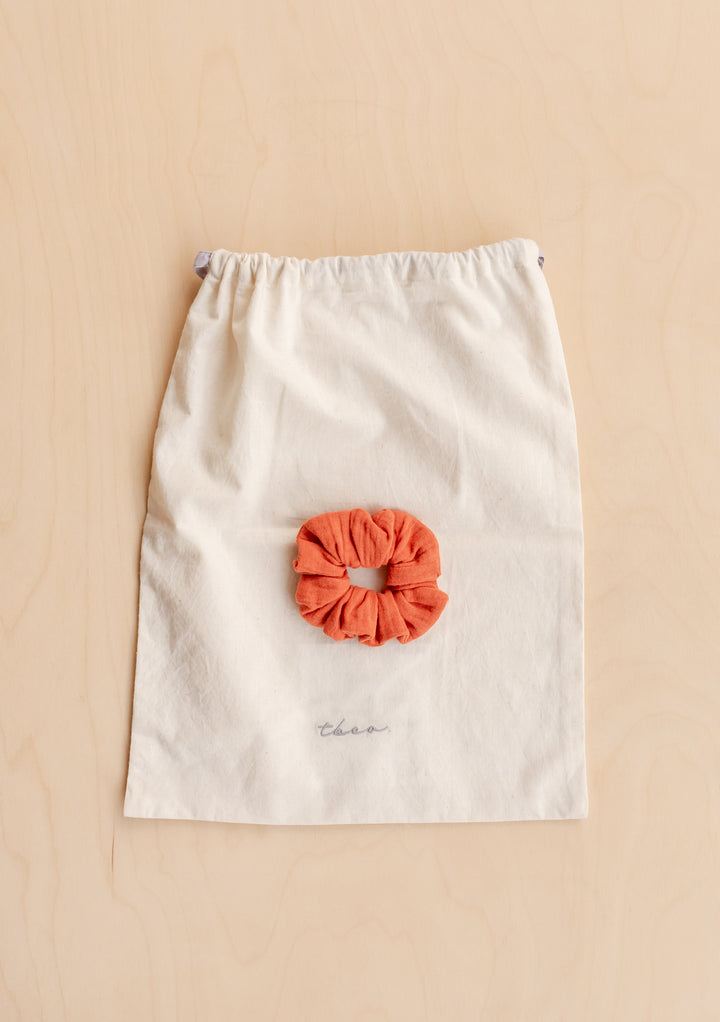 Cream TBCo drawstring bag with embroidered logo and rust scrunchie, complementing Cotton Pyjamas in Rust packaging.