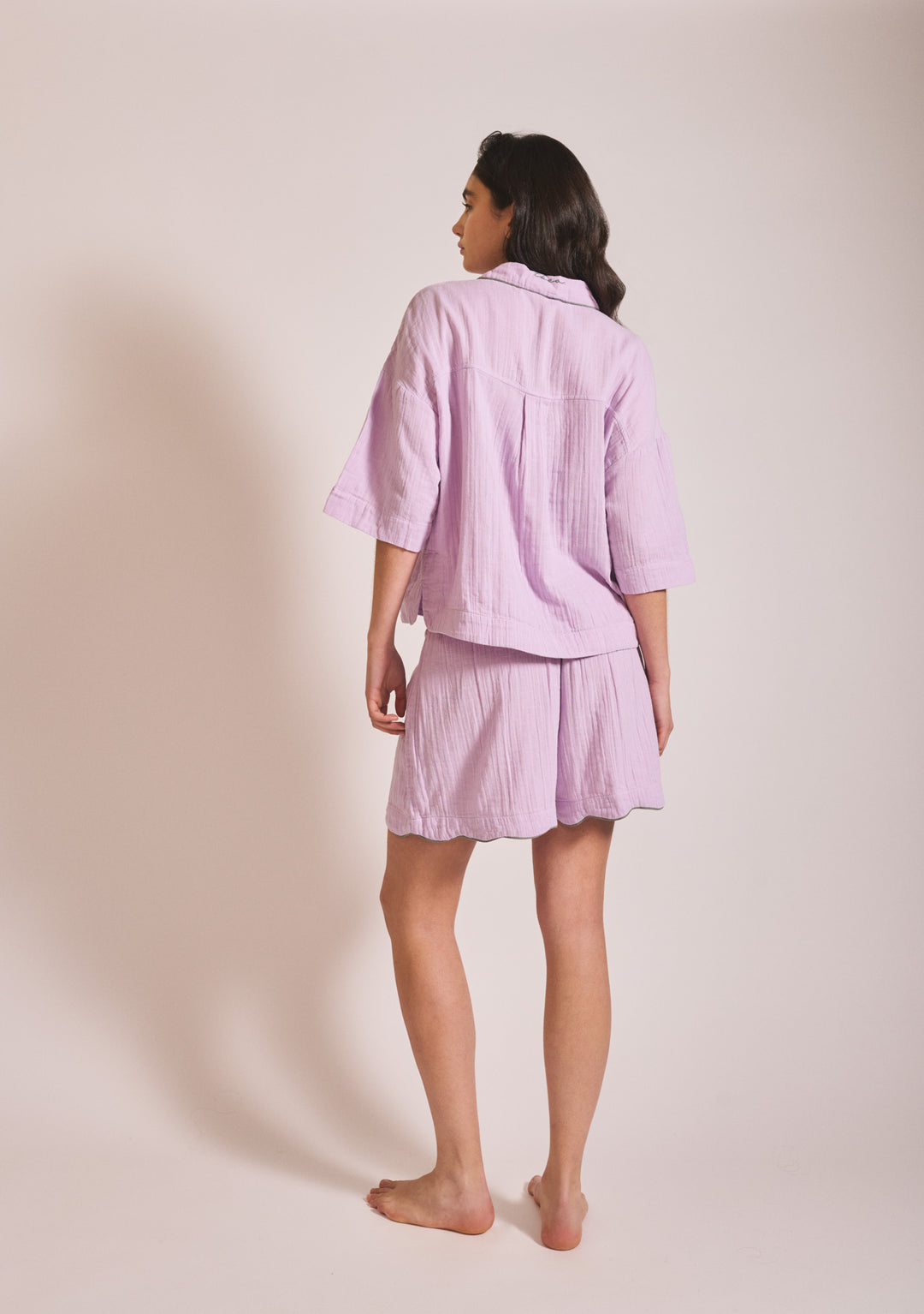 Woman standing barefoot in lilac Cotton Pyjamas in Lilac by TBCo, gallery position 3, portrait view, 1442x2048px.