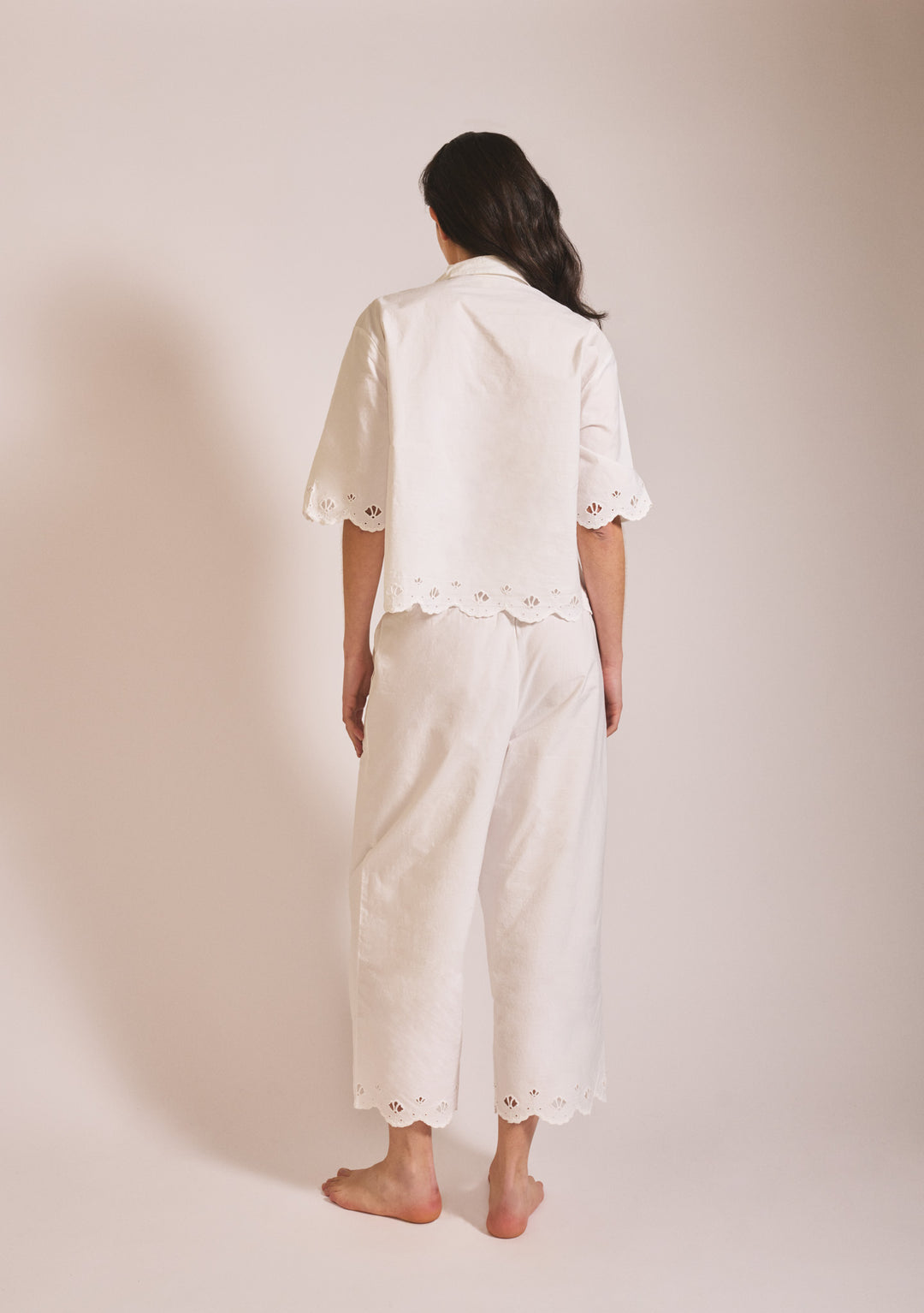 Back view of model wearing TBCo Cropped Cotton Pyjamas in White Shell with eyelet trim on sleeves and trousers