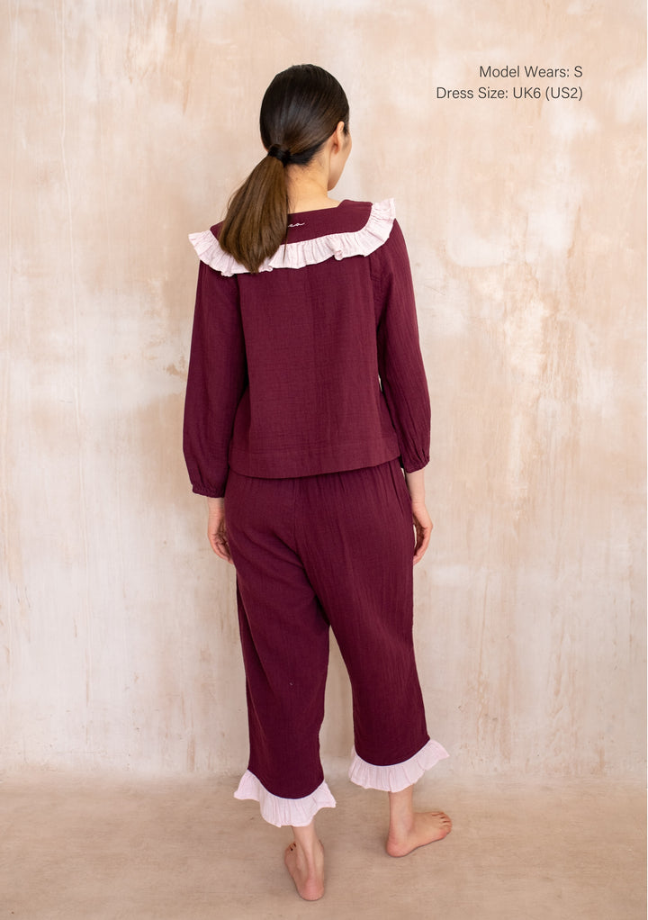 Back view of a Model wearing TBCo Cotton Pyjamas in Burgundy Ruffle with pink trim, featuring cropped trousers and pockets