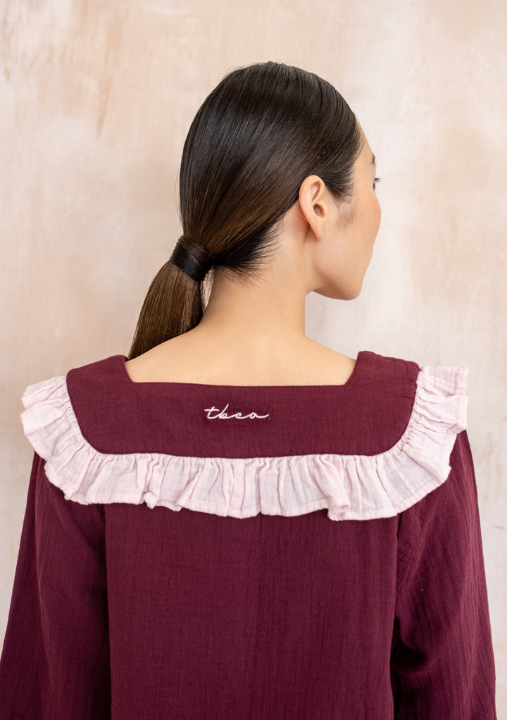 Back view of TBCo Cotton Pyjamas Burgundy Ruffle, featuring a sailor-style collar with pink ruffle and cursive TBCo embroidery, worn by a woman with a low ponytail.