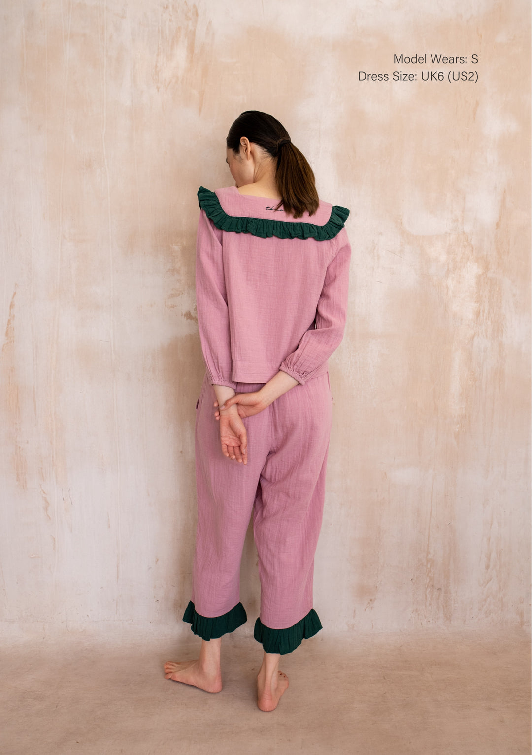Woman in TBCo Cotton Pyjamas in Pink Ruffle with green-trimmed collar and ankle cuffs, cropped pants, showcasing comfortable, stylish design.