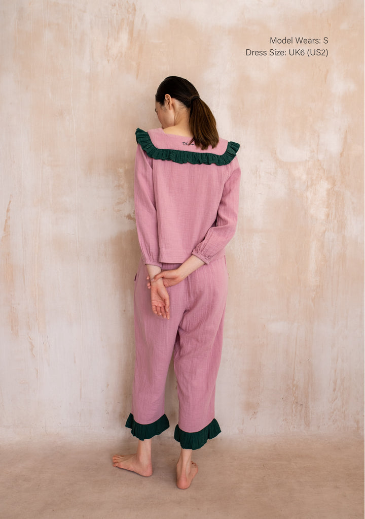 Woman in TBCo Cotton Pyjamas in Pink Ruffle with green-trimmed collar and ankle cuffs, cropped pants, showcasing comfortable, stylish design.