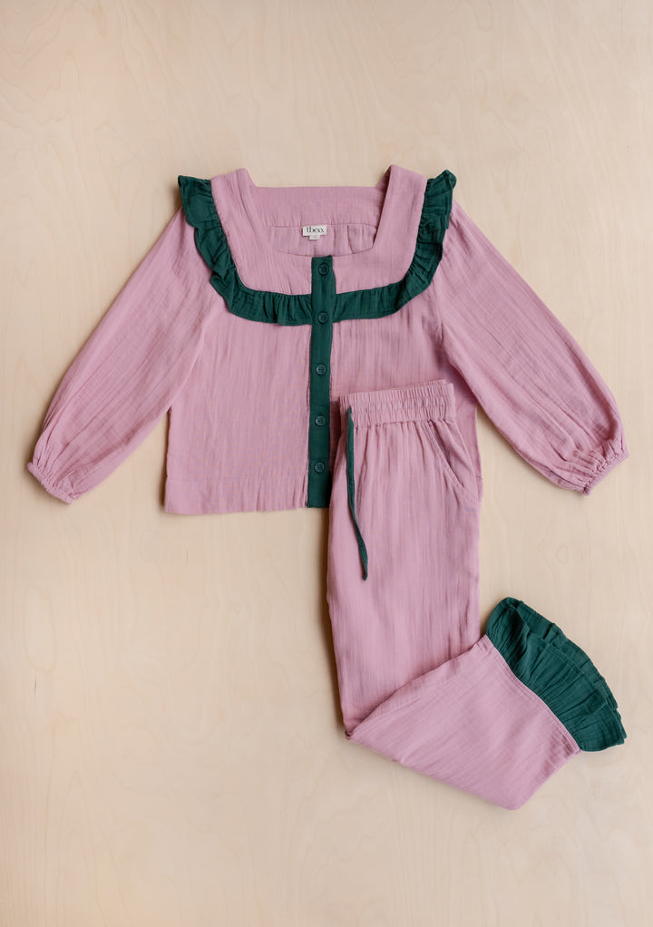 TBCo Cotton Pyjamas in Pink Ruffle: Soft pink two-piece set with dark green ruffles, button-front top, drawstring pants, and storage bag, designed in Edinburgh.