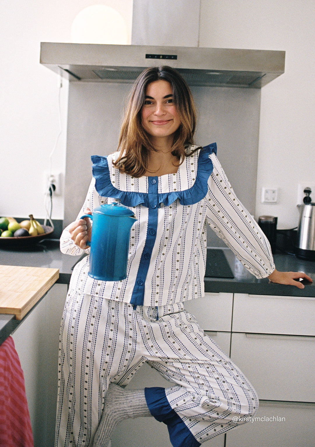 Woman wearing TBCo Cropped Cotton Pyjamas in Navy Ditsy floral holding a blue teapot in a bright kitchen setting
