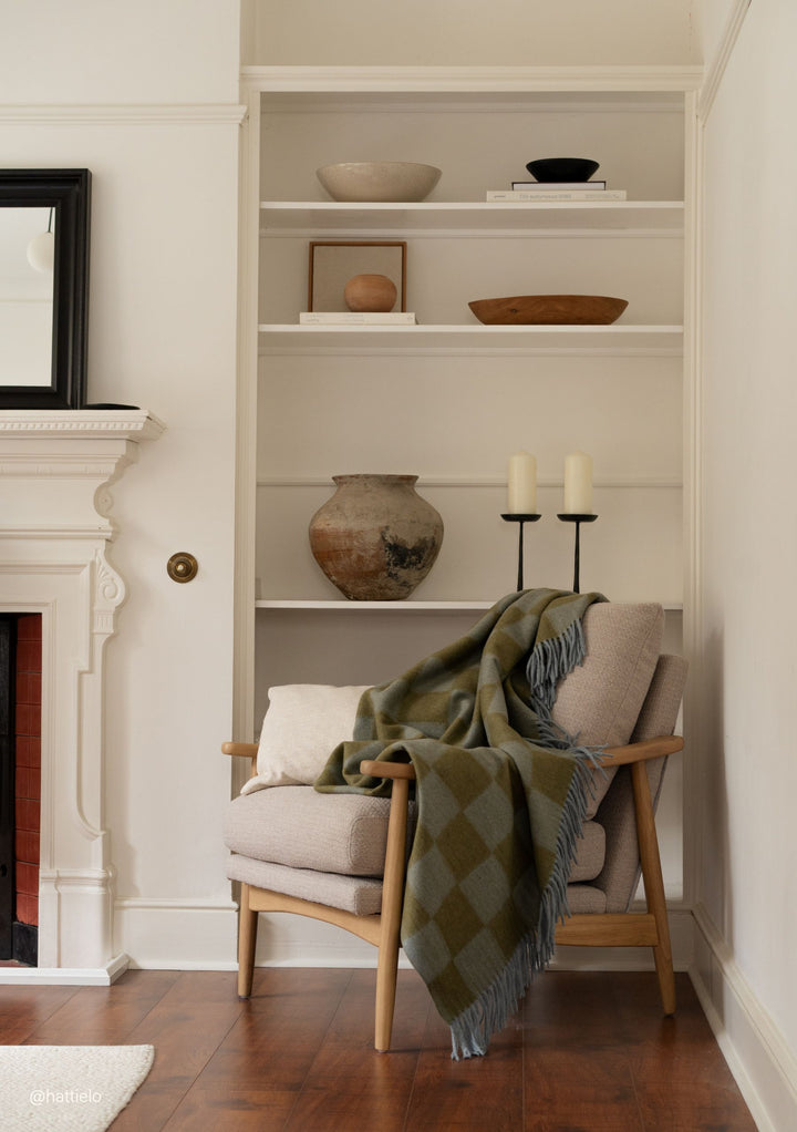 Cozy living room scene with TBCo Recycled Wool Blanket in Blue & Green Checkerboard draped over a beige armchair next to bookshelf