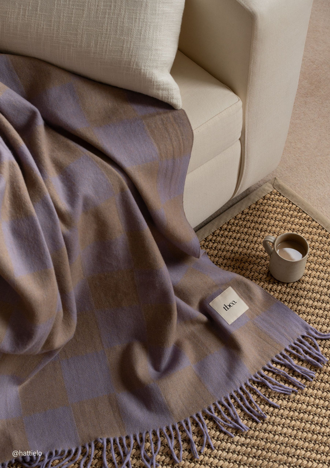 Recycled Wool Blanket in Lilac & Coffee Checkerboard by TBCo draped on cream sofa with fringed edge detail portrait view