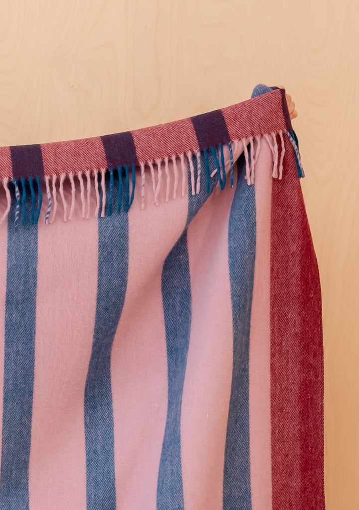 Close-up of fringed edge on TBCo Recycled Wool Blanket in Berry Frame Stripe with soft blue and berry stripes on pale wood background
