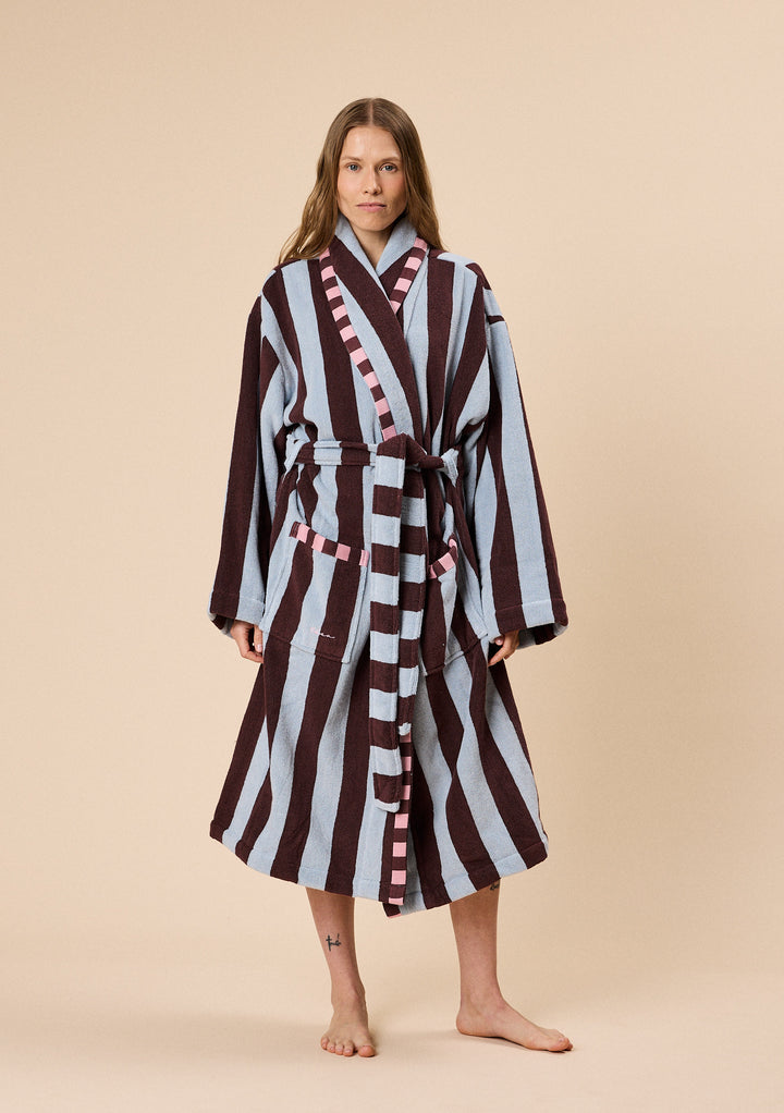 Model wearing TBCo Terry Cotton Bath Robe in Blue Stripe featuring wide vertical stripes and pink checked trim detail