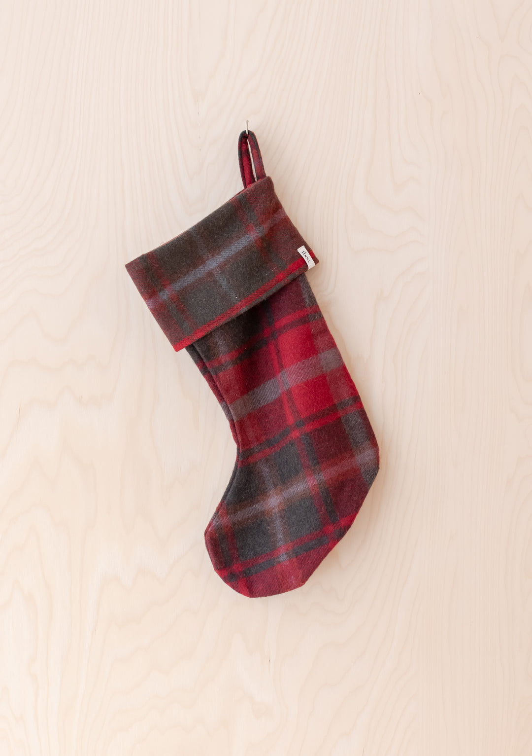 Recycled Wool Christmas Stocking in Dark Maple Tartan by TBCo hanging on light wood background in classic tartan pattern