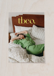 TBCo gift note with green cotton pyjama set with embroidered details, worn by a model lounging on soft, patterned bedding. A relaxed and breathable sleepwear essential for comfort and style.