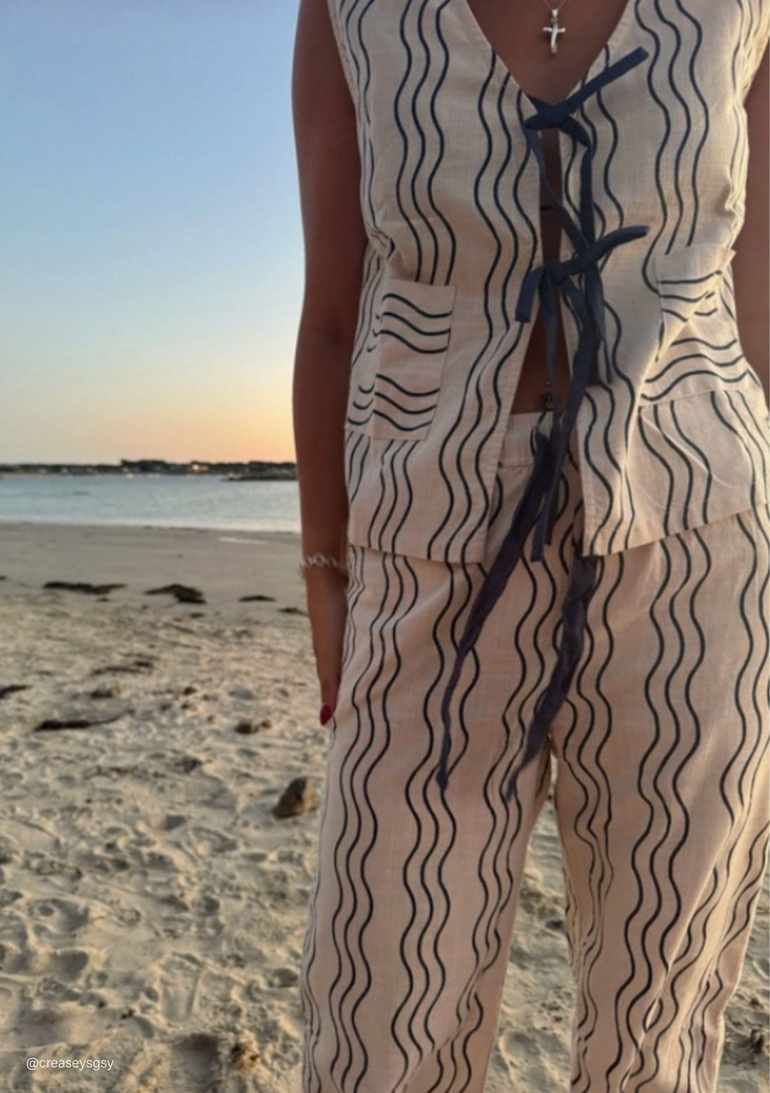Cotton Tie Top in Blue Wave by TBCo featuring navy wavy stripes and tie details in a beach setting at sunset