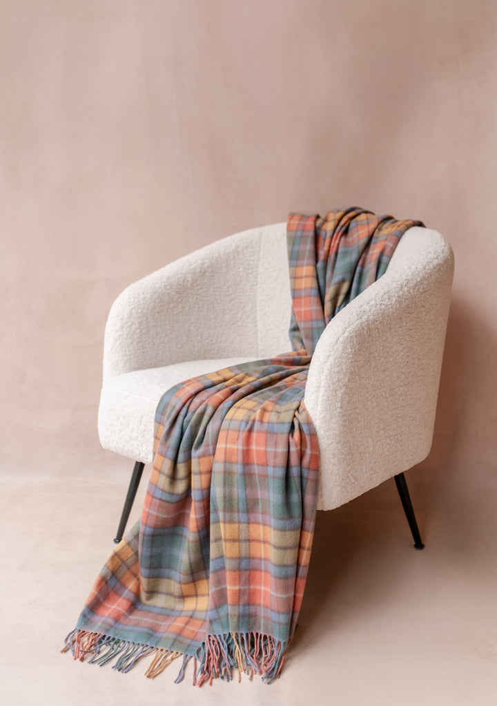 Soft TBCo Cashmere Blanket in Buchanan Antique Tartan draped over a white textured armchair with fringe detail