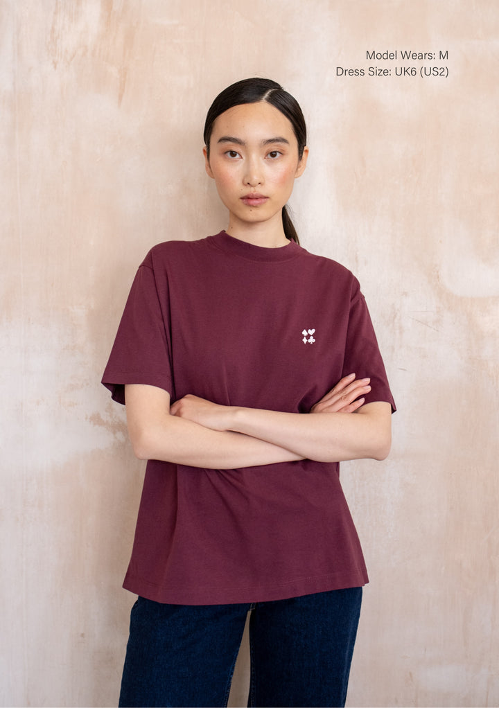 Front view of a model wearing the TBCo Cotton T-Shirt in Harlequin, showcasing a harlequin graphic with playing-card symbols on its burgundy on front