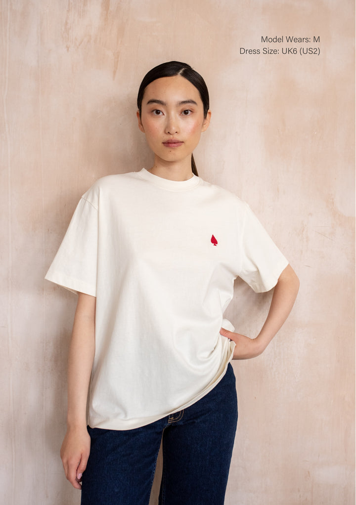 Model wearing the TBCo Cotton T-Shirt in Good Luck Cards, featuring embroidered red spade detail, paired with dark blue jeans.