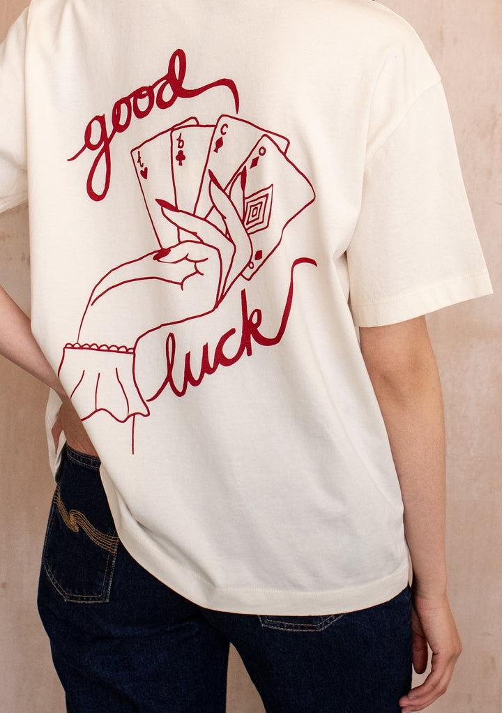 Model wearing the TBCo Cotton T-Shirt in Good Luck Cards, featuring a playing card graphic and good luck text, paired with dark blue jeans.